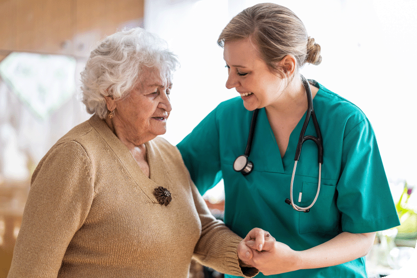 a female smiling carer assisting an older woman 