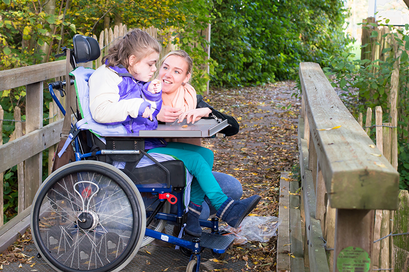 Carer outside with child in a wheelchair - Shutterstock